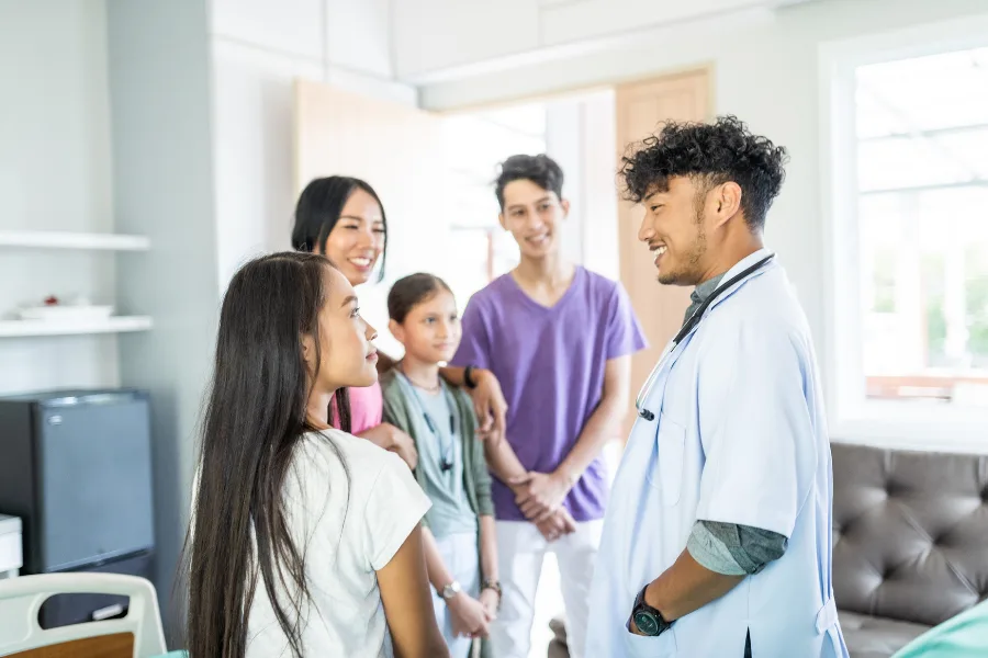 A doctor in a white coat talking with a family of four in a bright room