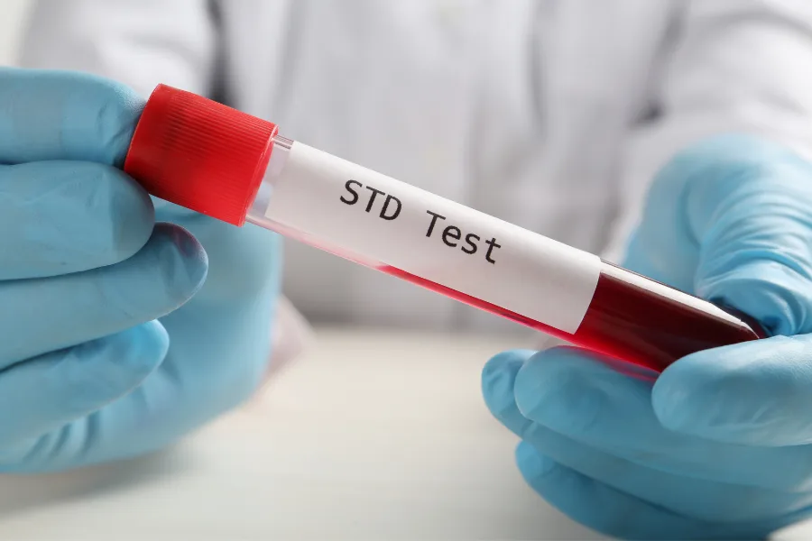 A gloved pair of hands holding a blood collection tube labelled "STD Test"