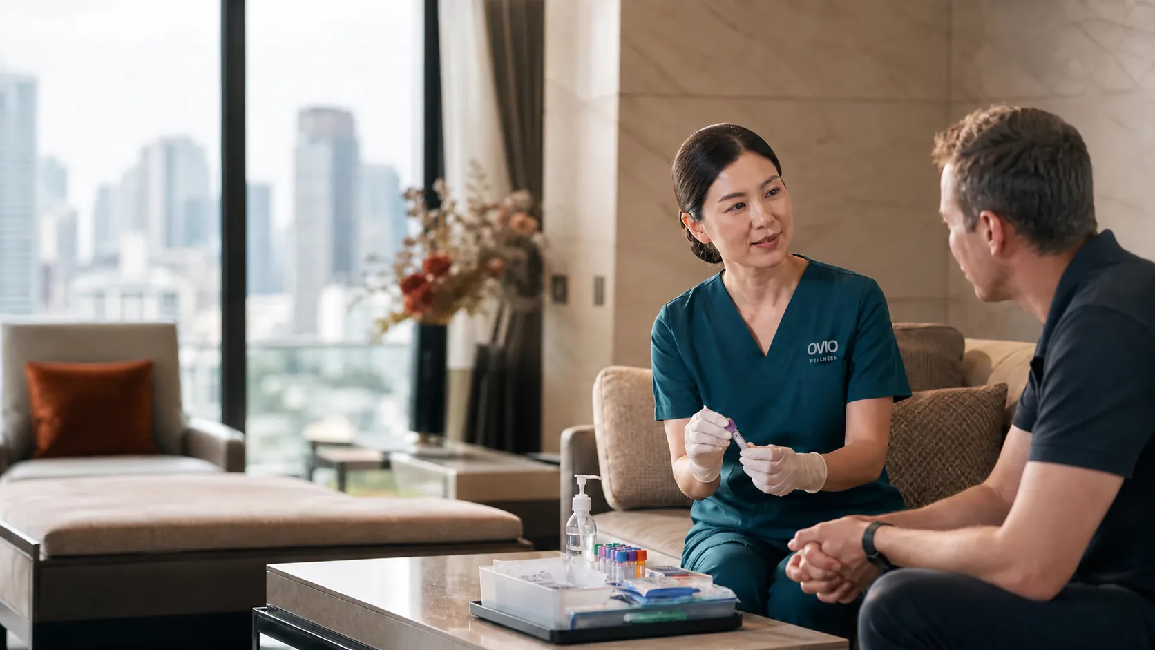 A nurse in Ovio Wellness scrubs showing a blood sample tube to a client during a home visit in Bangkok