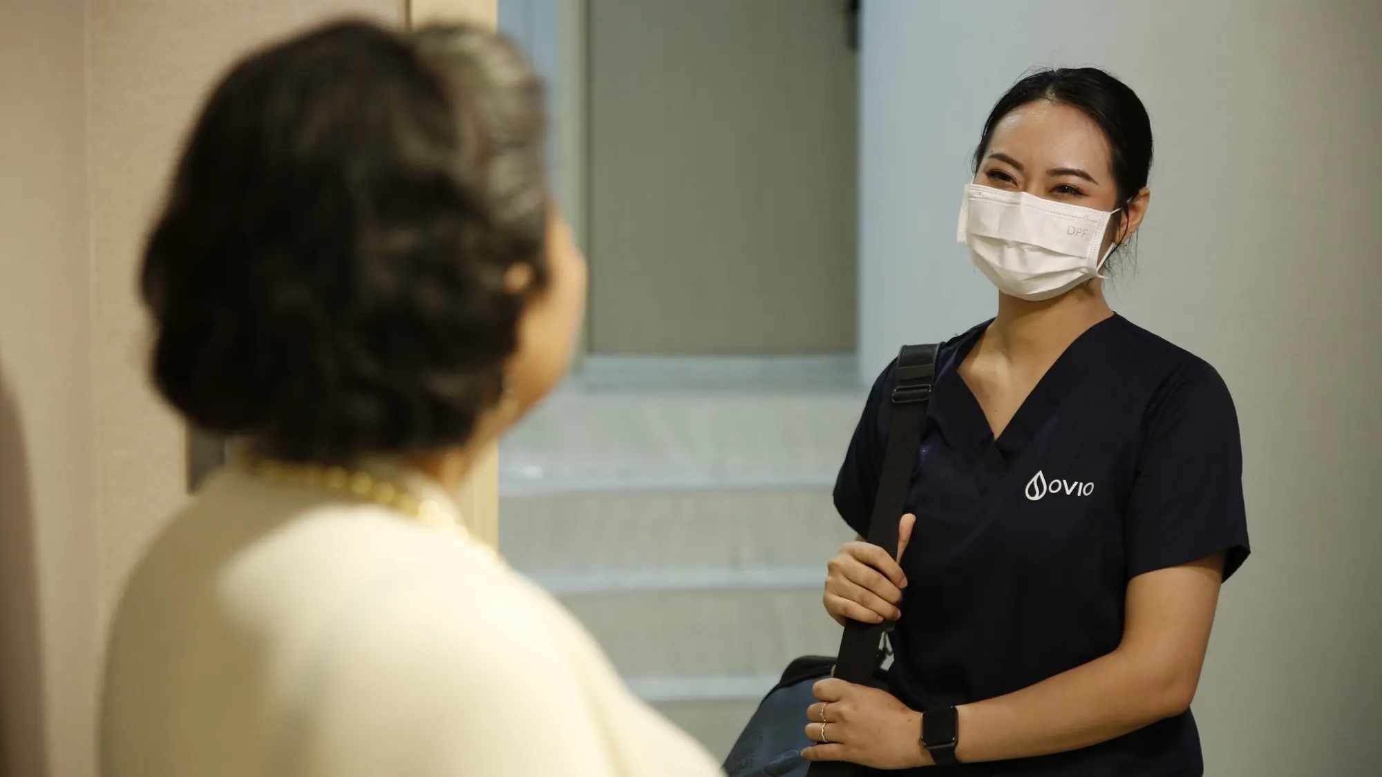 A smiling Ovio nurse with her medical bag arriving at a client's door in Bangkok